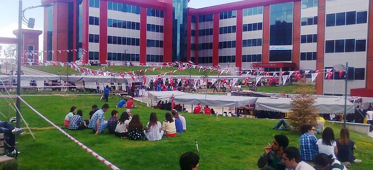 Na zdjęciu studenci siedzący na trawie przed campusem Uniwersytetu, 