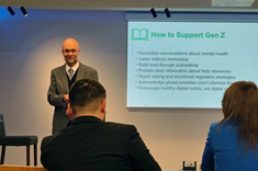Trzy osoby podczas dyskusji konferecyjnej, dwie widoczne od tyłu, jedna przodem, prezentująca referat, obok slajd zatytułowany: How to Support Gen Z, zdj. udostępnione przez uczestników