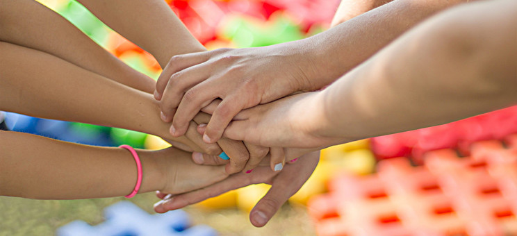 Zdjęcie przedstawia siedem rąk - dłonie ułożone są jedna na drugiej,