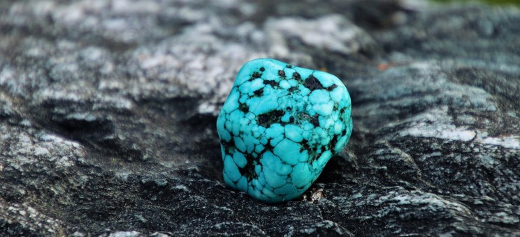 Zdjęcie przedstawia bryłkę naturalnego turkusu leżącą na skale,